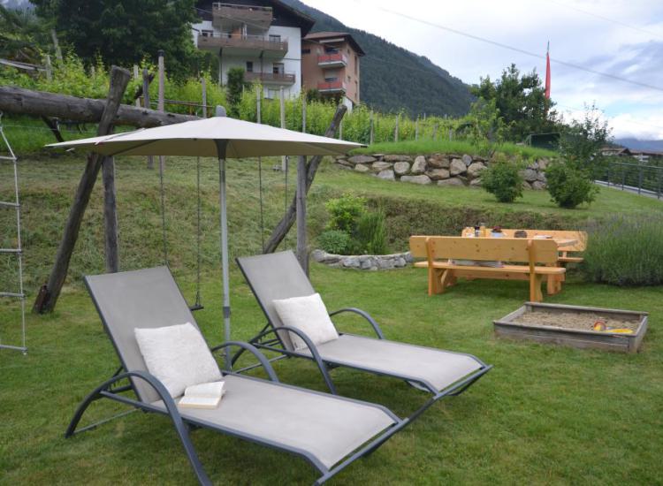 Sedie a sdraio con ombrellone e sabbiera nel giardino del Langeshof in Alto Adige