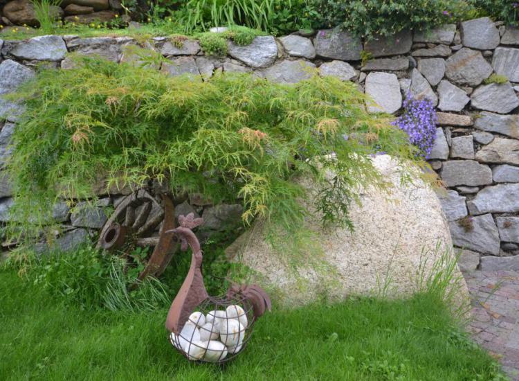 Decorazione rustica da giardino con vecchio cesto di ferro, muro in pietra naturale e arbusti ornamentali al Langeshof